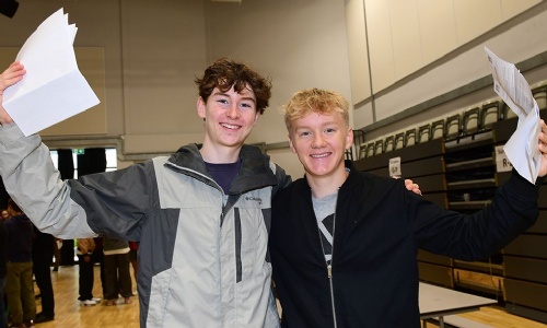 Two students smiling and holding up their GCSE results